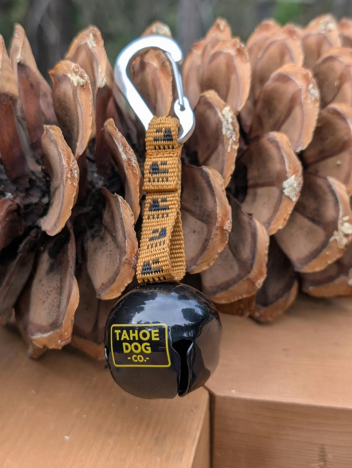 Black Trail Bell showing the Tahoe Dog Co. logo, golden-brown mountain strap, and metal carabiner.