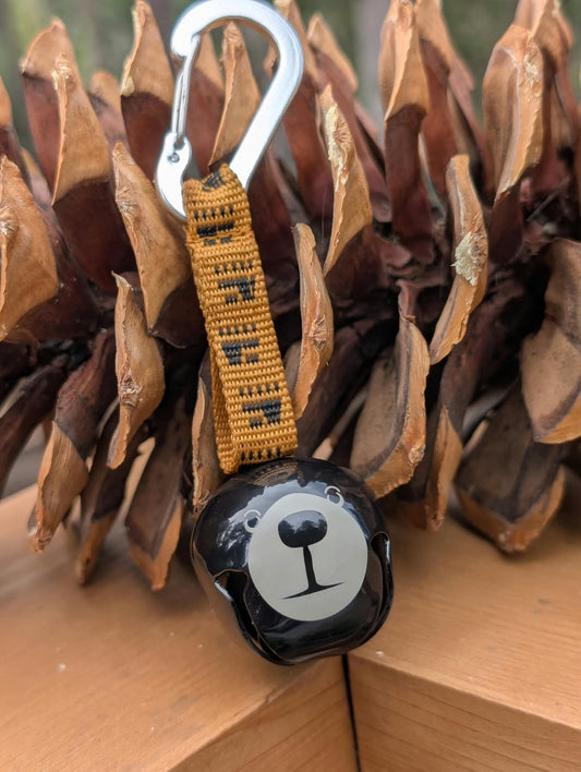 Black Trail Bell for dogs featuring the Tahoe Dog bear, golden-brown mountain strap, and metal carabiner.
